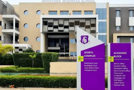 Here is a **125–140 character SEO-optimized alt text** for this campus image: ### ✅ **ALT Text (125–140 characters)** *Front view of an MBA college campus with signage for the sports complex and academic block, showing modern infrastructure and student facilities.*